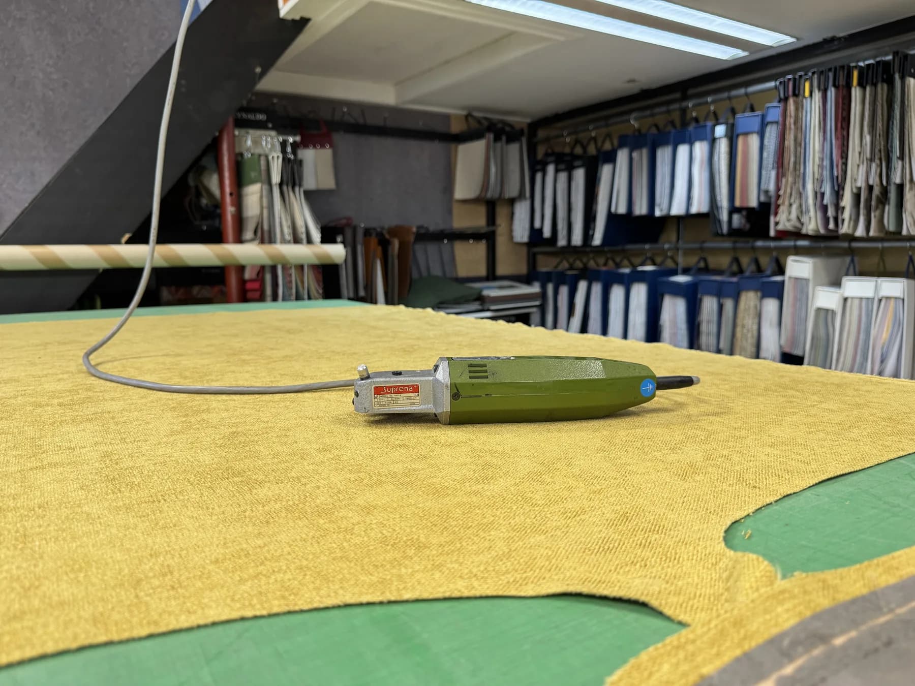 Werktafel met gele stof en snijgereedschap in Jans werkplaats